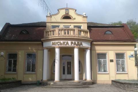 Фасад жовтавої будівлі міської ради з білими колонами та гербом