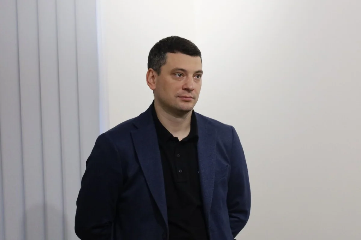 Андрій Годик у синьому піджаку стоїть на тлі світлої стіни