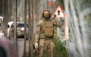 Військовий у камуфляжі та бронежилеті перевіряє антидронову сітку біля дороги