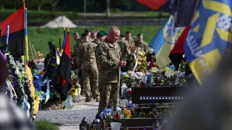 Військовий у камуфляжі стоїть серед могил із вінками та прапорами на Личакові