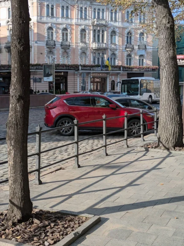 Червоний кросовер на бруківці біля історичної будівлі з українським прапором