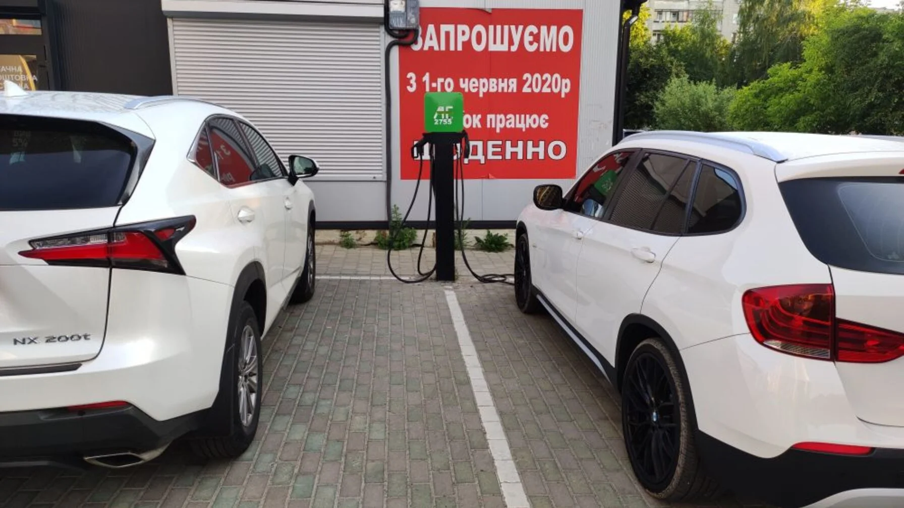 Два білі електромобілі припарковані біля зарядної станції з червоним оголошенням