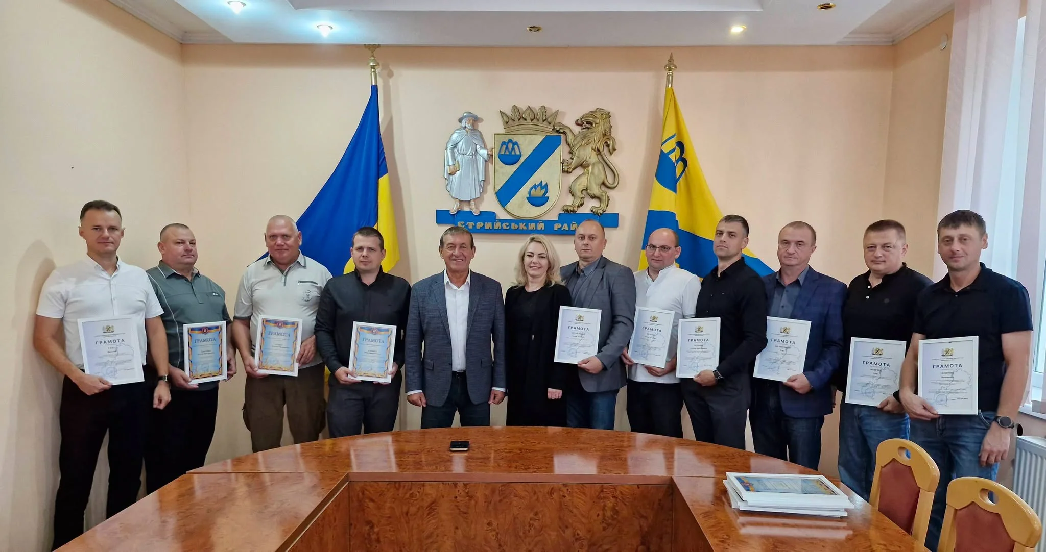 Група людей з грамотами біля герба Стрийського району в залі адміністрації