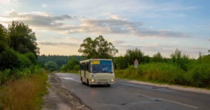 Кремовий автобус маршруту 150 їде сільською дорогою серед дерев