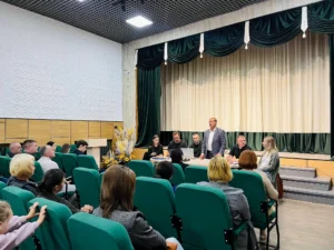 Зустріч у актовій залі: люди в кріслах слухають виступ за столом на сцені