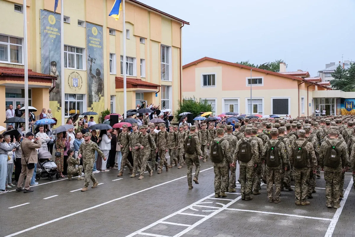 Першокурсники ліцею Героїв Крут у камуфляжі строєм перед будівлею під дощем у Львові