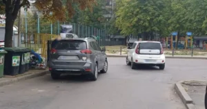Сірий кросовер і білий Kia стоять на вулиці біля смітників і майданчика
