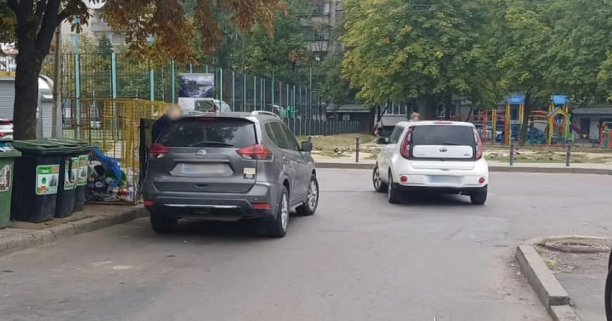 Сірий кросовер і білий Kia стоять на вулиці біля смітників і майданчика